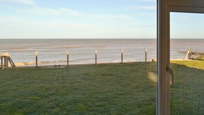 A view of the ocean from a window overlooking a grassy area with a fence and wooden posts.