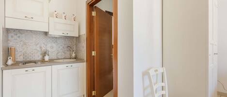A kitchen with white cabinets, a wooden door, and a white chair.