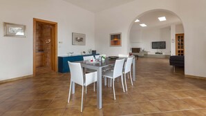 A spacious living area with a dining table and chairs, a kitchen in the background, and a TV mounted on the wall. - 2506 Villa Sorriso by Barbarhouse (Lecce)