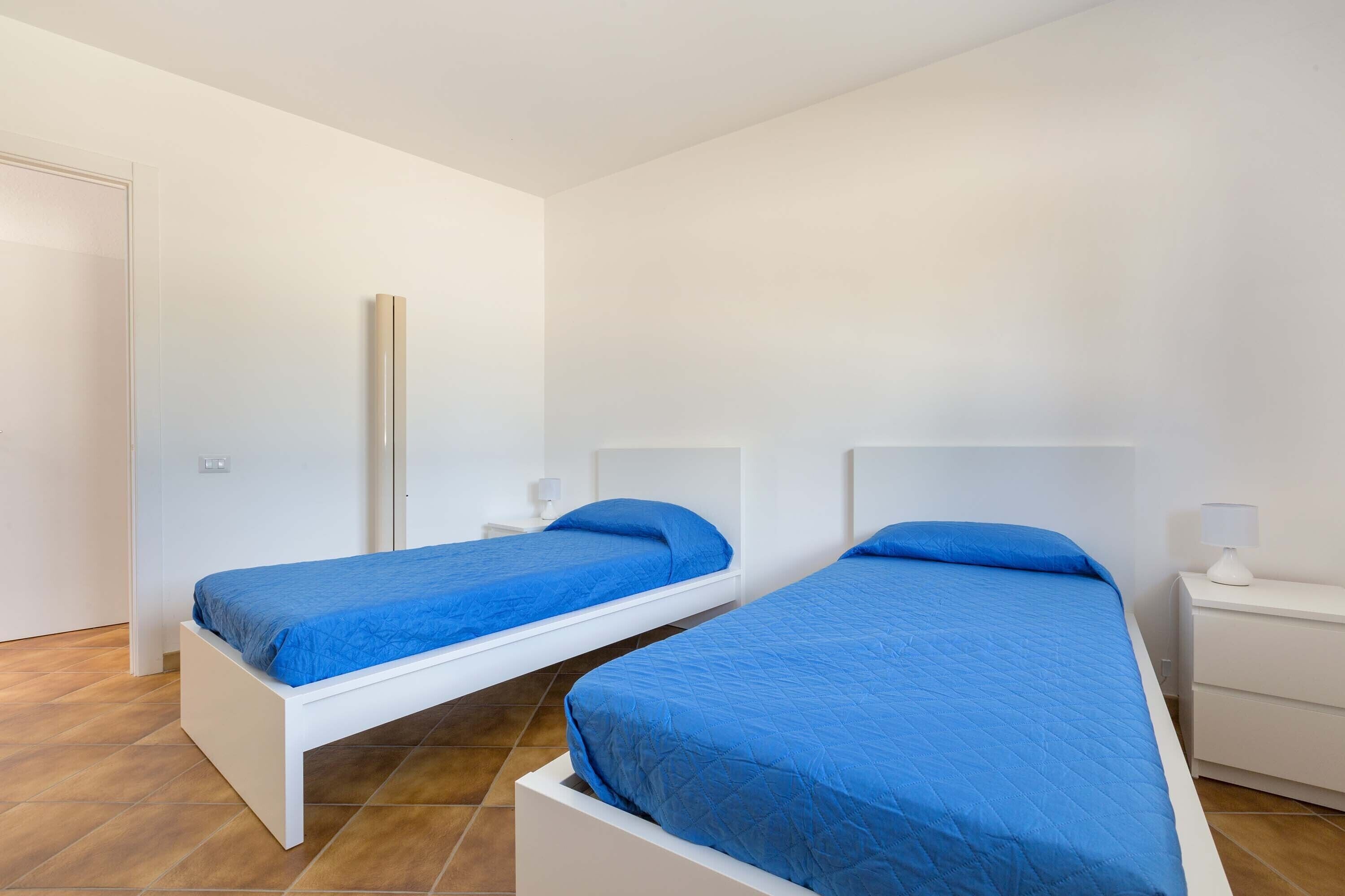 Een kamer met twee eenpersoonsbedden, witte nachtkastjes en een witte kledingkast.