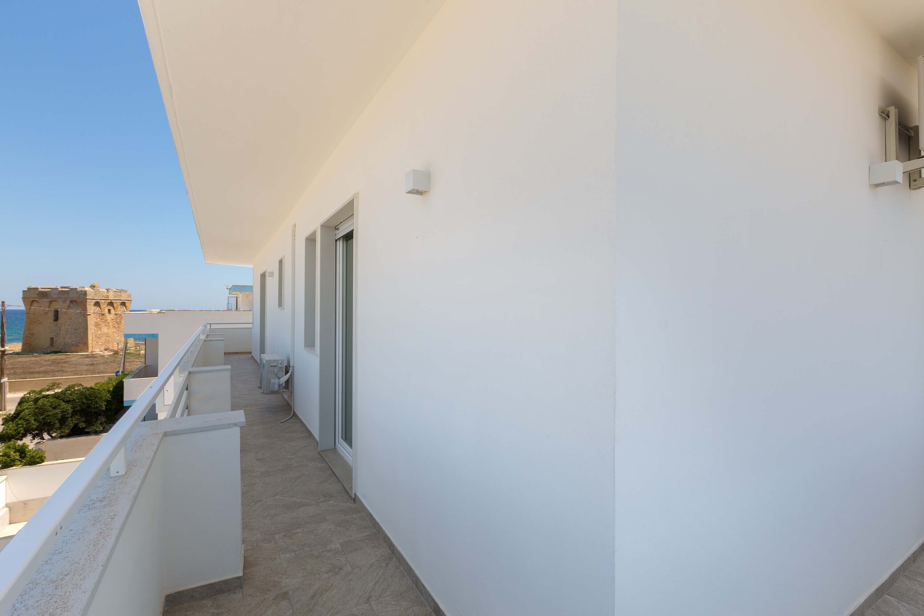 A narrow balcony with a clear view of the sea and a historic building in the background.