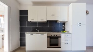 A modern kitchen with white cabinets, a black tiled backsplash, a stove, and a clock on the wall. - 1852 Villa Nataly - Primo Piano by Barbarhouse (Lecce)