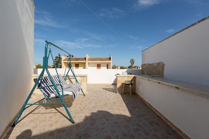 A rooftop terrace with a swing set, a small table, and a chair.