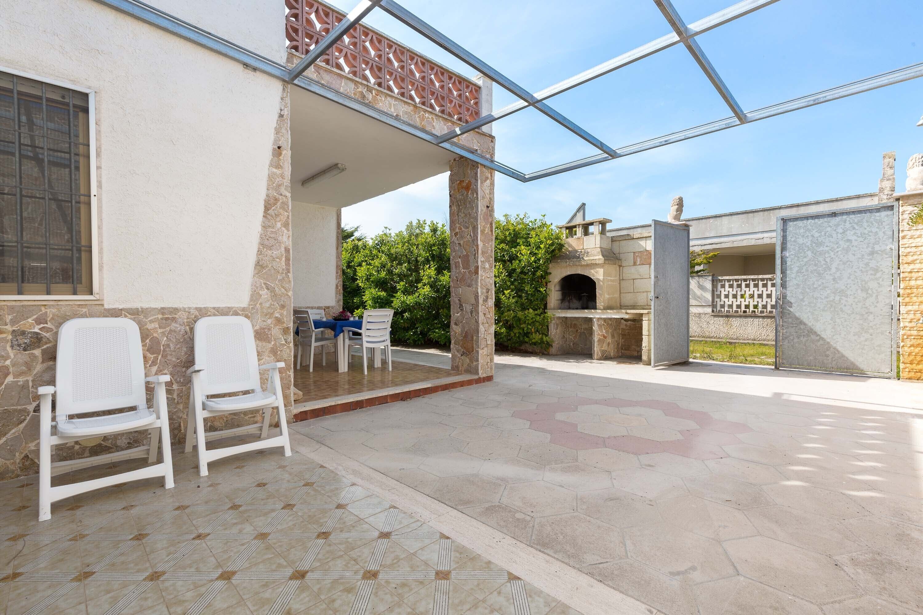 Un patio al aire libre con dos sillas blancas, una mesa y una zona con paredes de cristal.