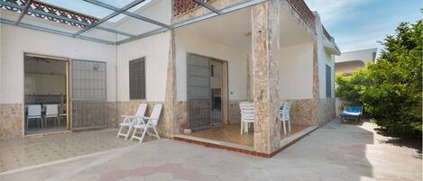 A covered patio area with hexagonal tile flooring, white chairs, and a glass enclosure.