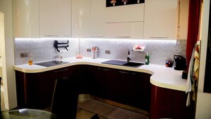 A modern kitchen with white cabinets, a black countertop, and a tiled backsplash. - Modern and Homely Apartment in Marsaskala (Marsaskala)
