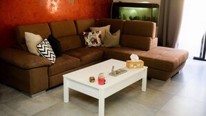 A brown sectional sofa with patterned cushions, a white coffee table with a tissue box and small items, and a red textured wall with a map. - Modern and Homely Apartment in Marsaskala (Marsaskala)