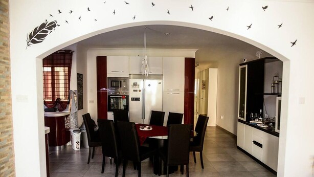 A modern kitchen and dining area with a central island, white cabinets, and a red dining table. - Modern and Homely Apartment in Marsaskala (Marsaskala)
