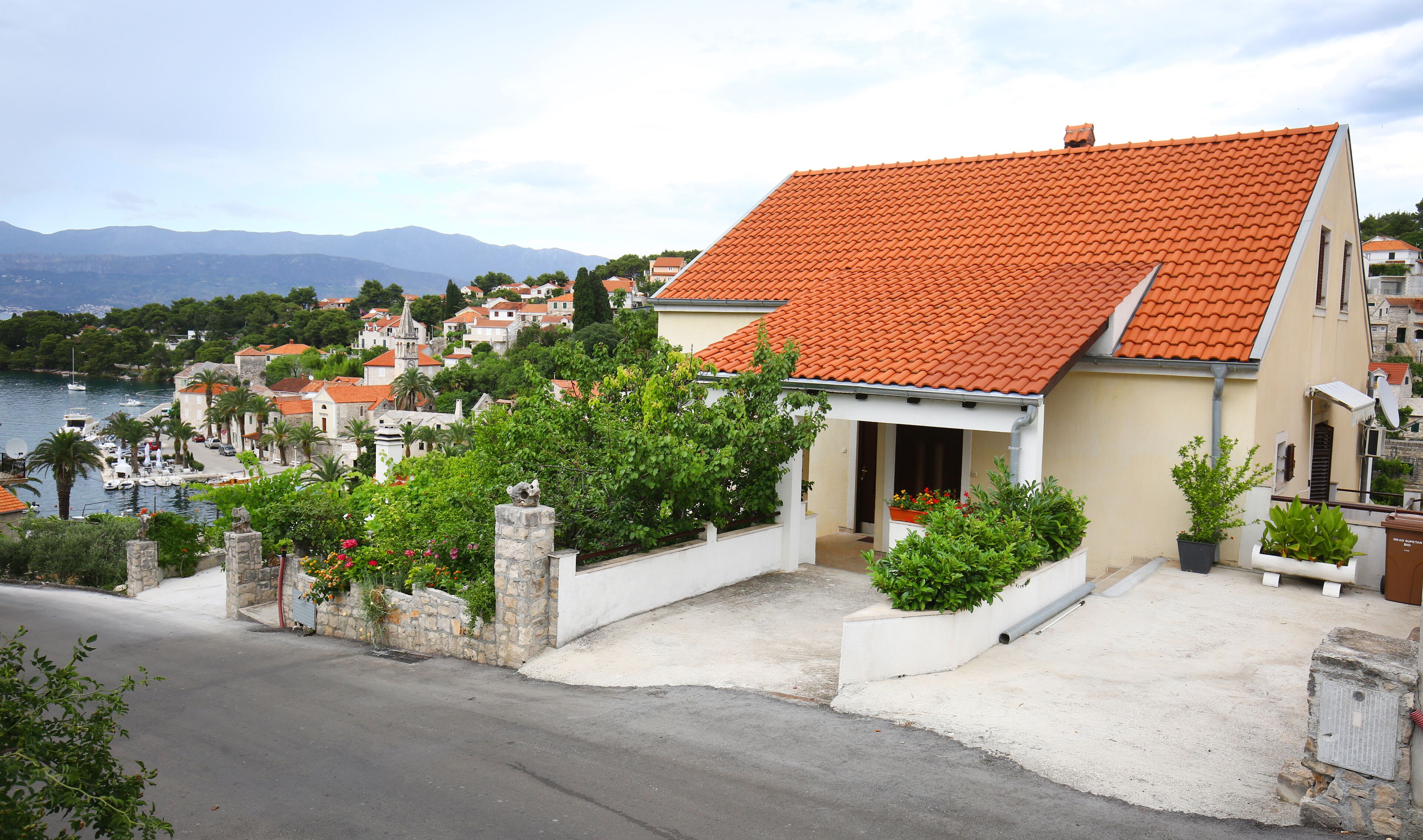 A coastal building with a red-tiled roof, surrounded by greenery and a view of the sea.