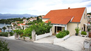 Ein Küstengebäude mit rotem Ziegeldach, umgeben von Grün und Blick auf das Meer.
