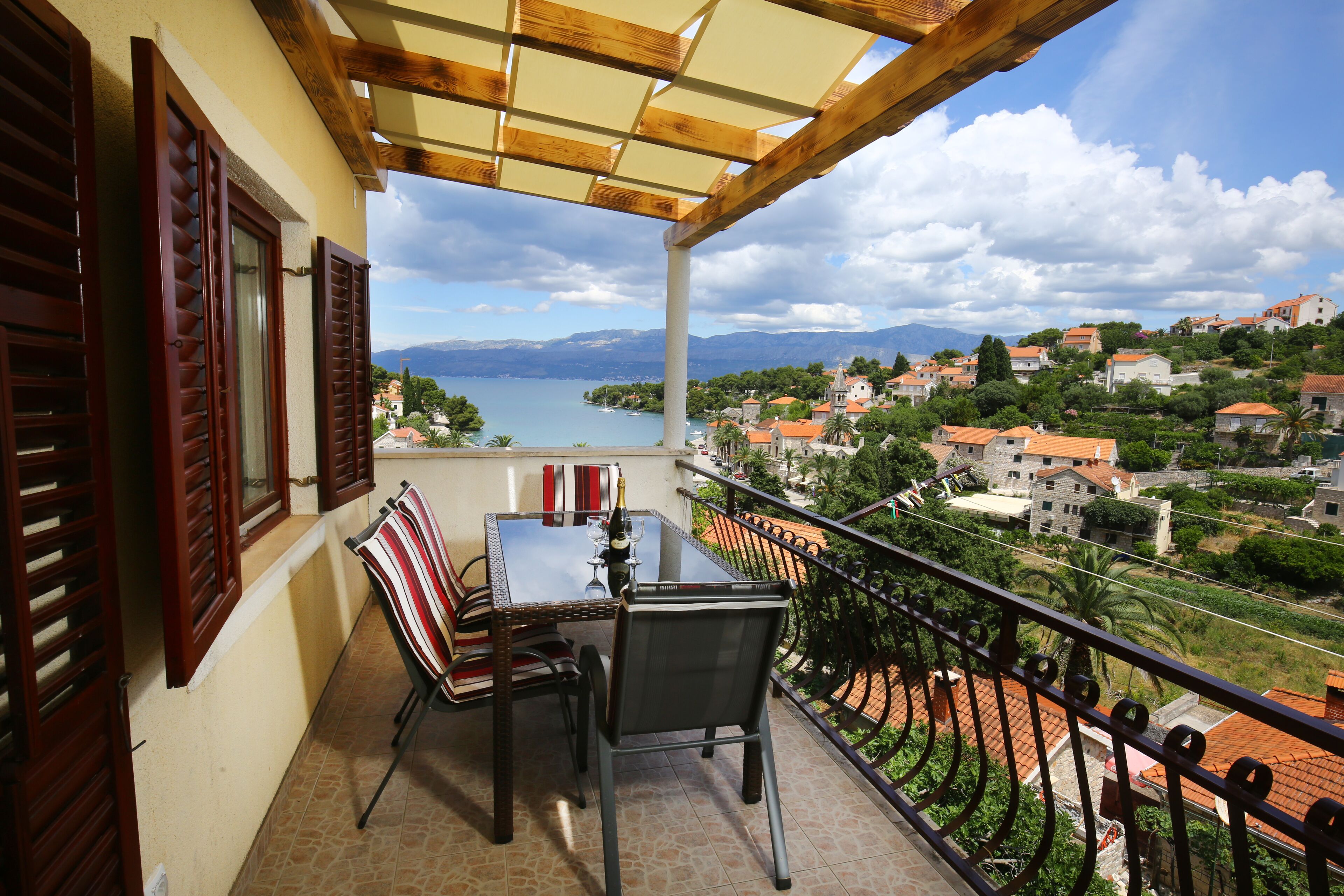 Een balkon met een tafel en stoelen, uitzicht op een meer en huizen op de achtergrond.