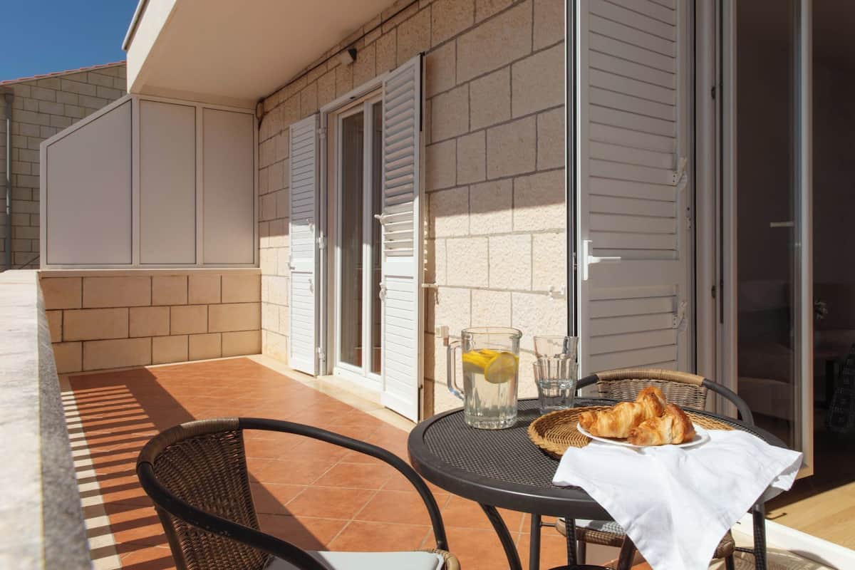 An outdoor patio with a table set for two, a glass pitcher with a lemon, and a basket of croissants.