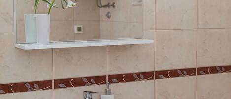 A bathroom with a white sink, a mirror above it, a white vase with flowers, and a toilet.