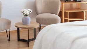 Een hotelkamer met een bed, twee stoelen, een klein rond tafeltje met een bloevas en een houten bureau.