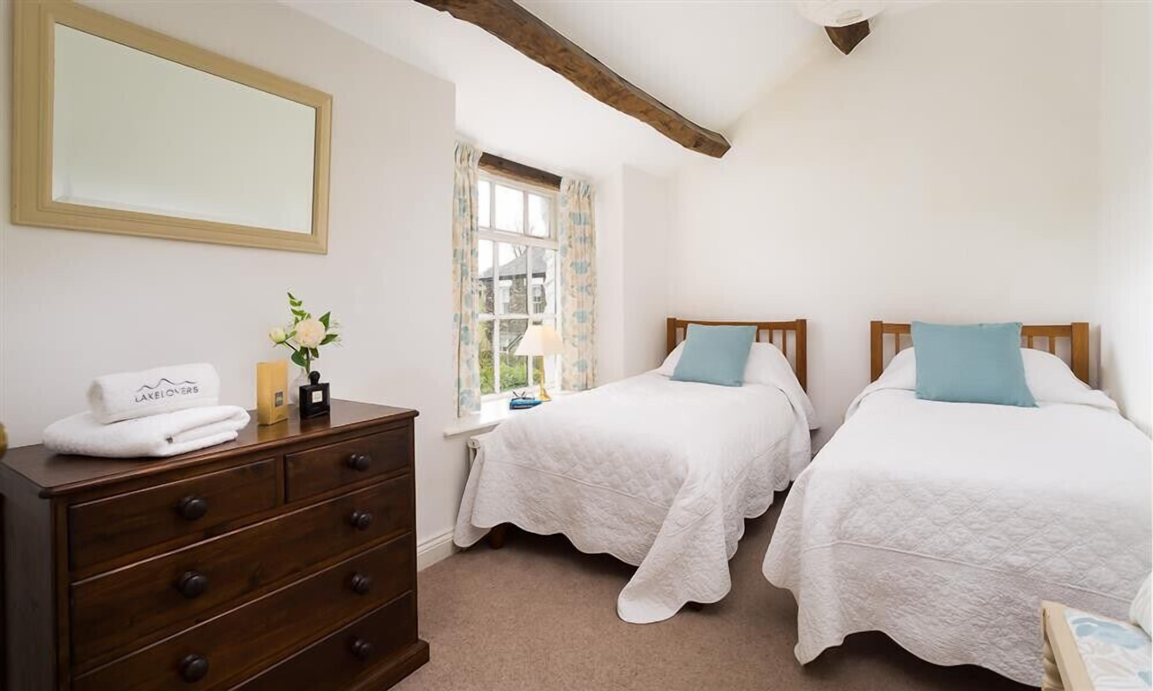 Un dormitorio con dos camas individuales, un aparador de madera, un espejo y una ventana con cortinas.