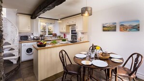 A compact kitchen with a central island, a dining area with four chairs, and a hanging light fixture. - Camellia Cottage (Kendal)