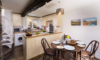 A compact kitchen with a central island, a dining area with four chairs, and a hanging light fixture.
