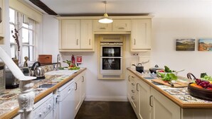 A kitchen with white cabinets, a double oven, and a countertop with fruits and vegetables. - Camellia Cottage (Kendal)