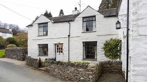 A white two-story house with a stone wall and a small garden. - Camellia Cottage (Kendal)
