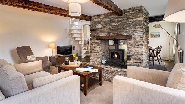 A cozy living room with a stone fireplace, comfortable seating, and a television. - Camellia Cottage (Kendal)