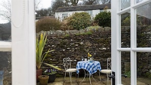 A stone wall, a table with a blue checkered tablecloth, and potted plants in a courtyard. - Camellia Cottage (Kendal)