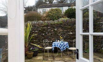 A stone wall, a table with a blue checkered tablecloth, and potted plants in a courtyard.
