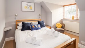 Un lit bien fait, avec du linge de lit blanc et des serviettes pliées, une tête de lit en bois et un tableau représentant un vélo accroché au mur.