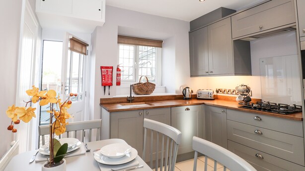 Une cuisine moderne avec des meubles gris, un plan de travail en bois et un coin repas avec une table blanche mise pour deux personnes.