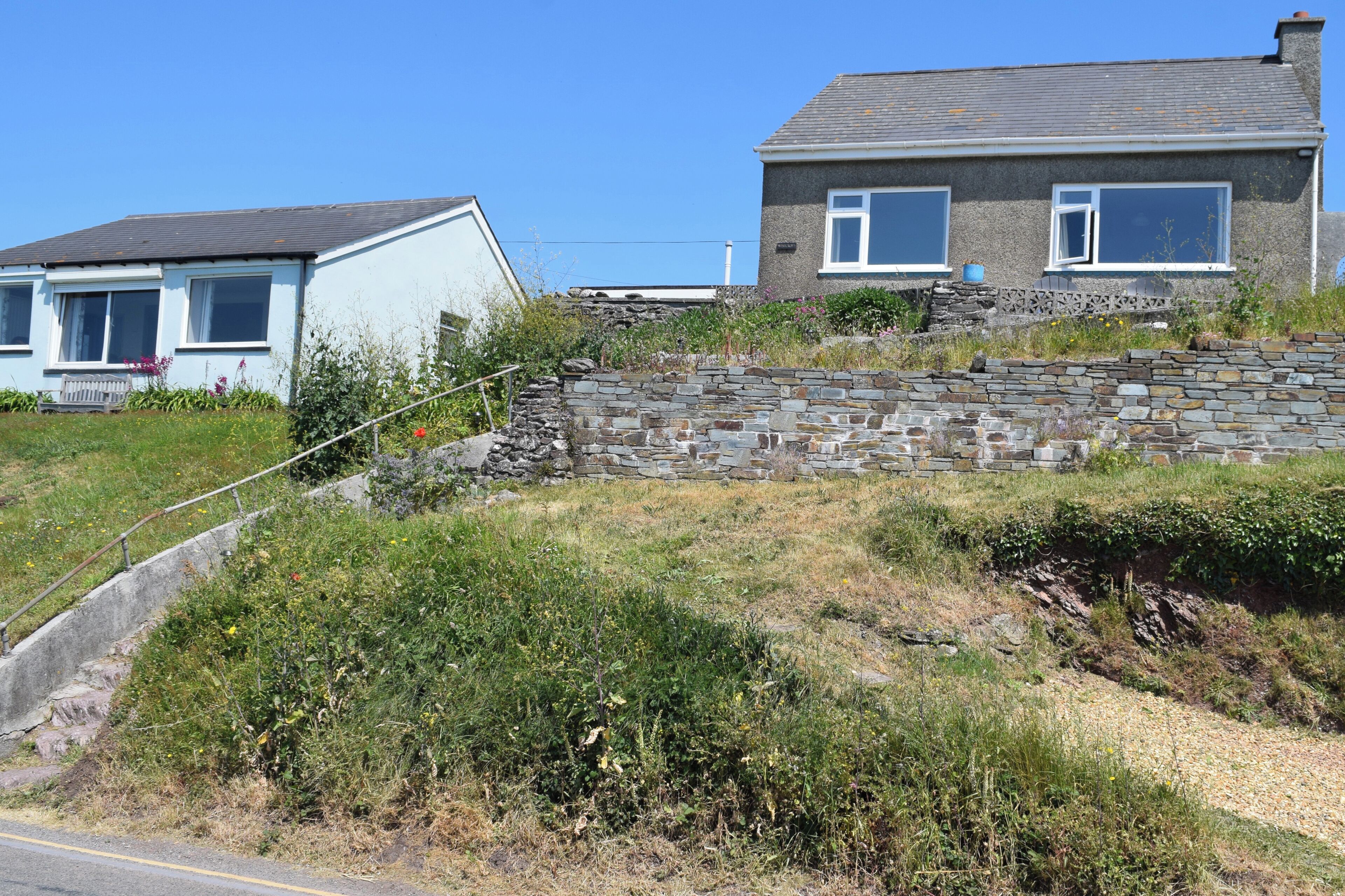 Une maison à deux étages, dotée d’un mur de soutènement en pierre et d’une pelouse devant.