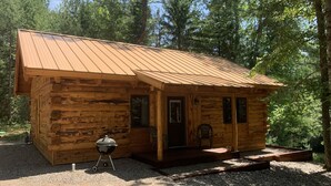 A small wooden cabin with a metal roof, a porch, and a grill outside.