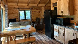 A cabin interior with wooden walls, a dining table, a refrigerator, a microwave, and a ceiling fan.