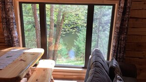 A cabin interior with a large window, wooden furniture, and a view of a forest.