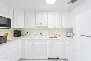 A modern kitchen with white cabinetry, a built-in microwave, a coffee maker, and a dishwasher. - Beachfront Condo | Pool, Tennis & Fitness Center (Marco Island)