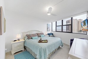 A bedroom with a bed, bedside tables, a desk, and a window with a view of buildings. - Beachfront Condo | Pool, Tennis & Fitness Center (Marco Island)