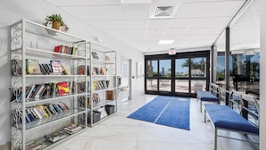A library with bookshelves, a blue carpet, and a view through the door. - Beachfront Condo | Pool, Tennis & Fitness Center (Marco Island)
