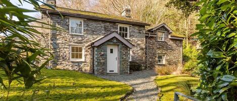 A stone house with a gravel driveway and a metal gate.