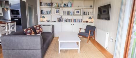 Una sala moderna con un sofá gris, una mesa de centro blanca y una estantería llena de libros.