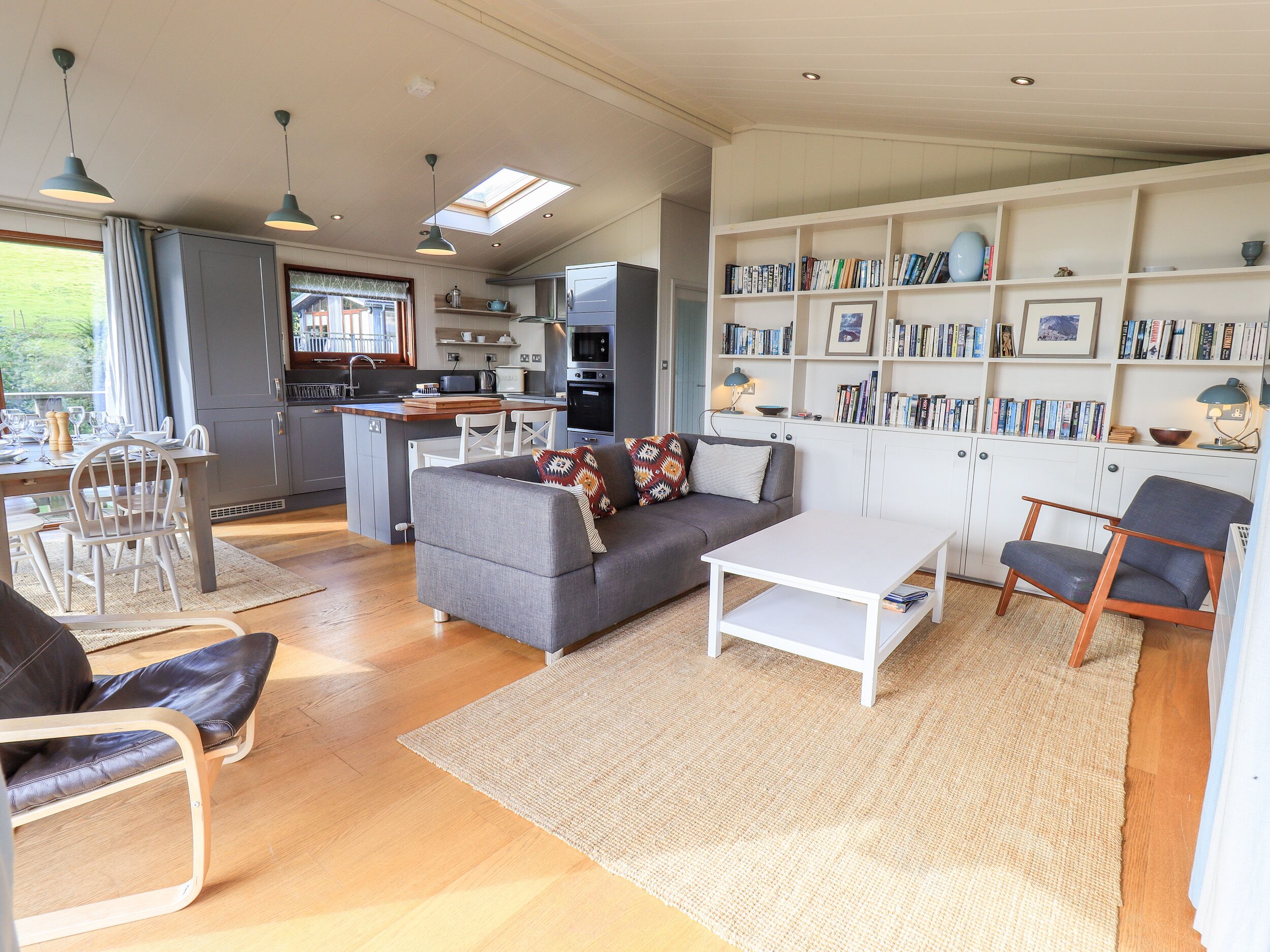 A modern living space with a kitchen, dining area, and a bookshelf filled with books.