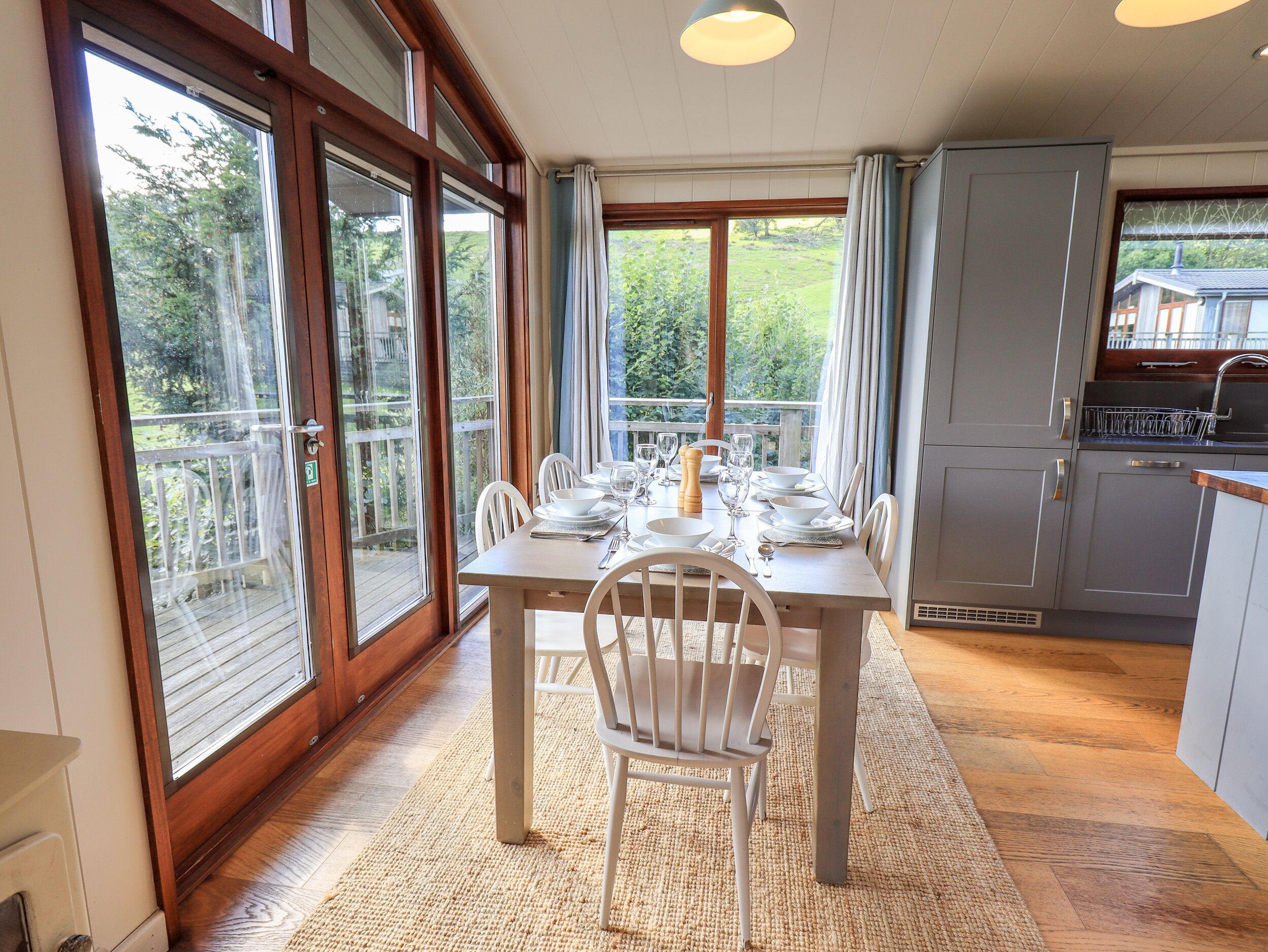 A dining area with a table set for four, large windows, and a kitchen area.