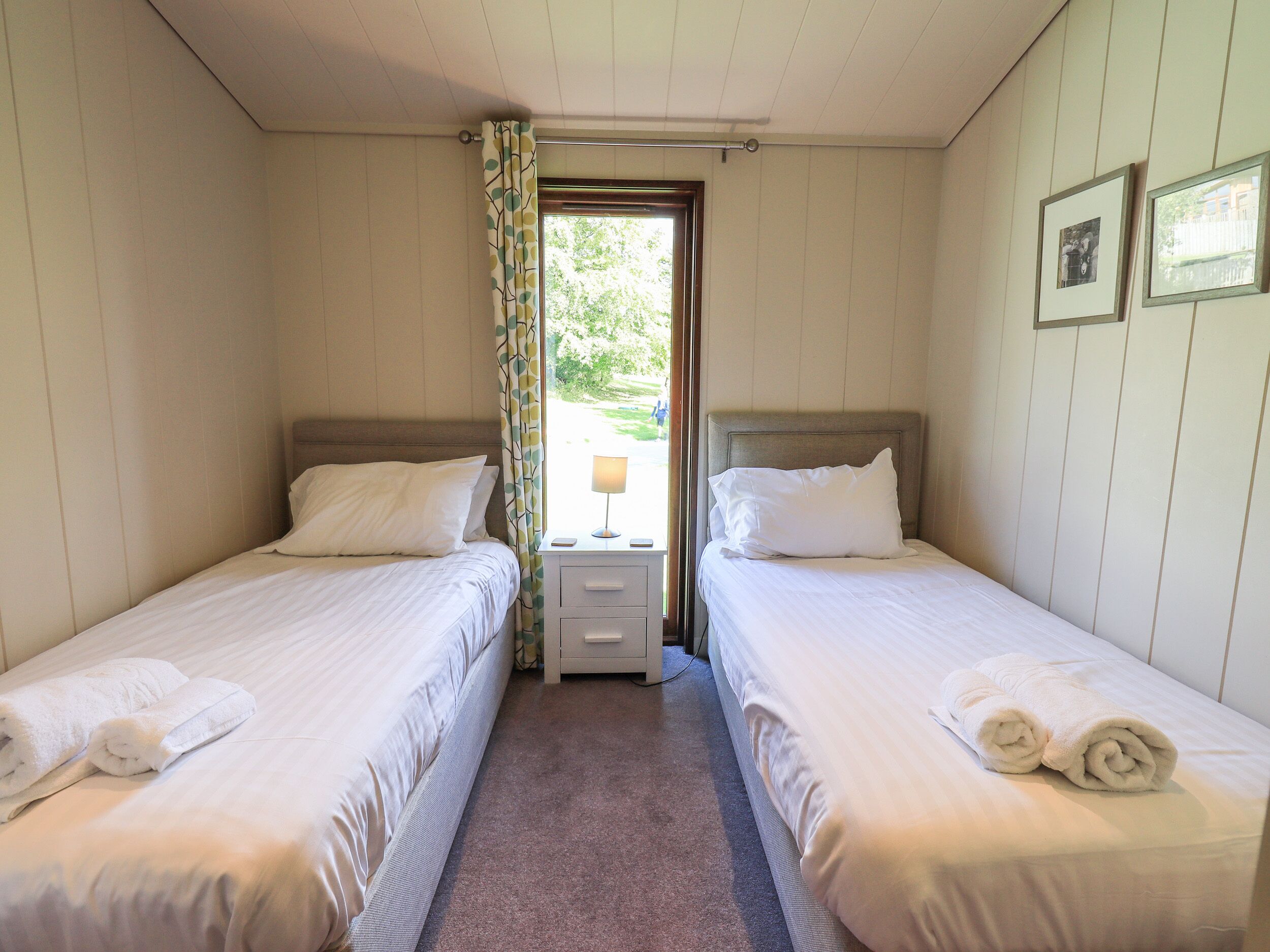 A room with two beds, a nightstand, and a window with curtains.