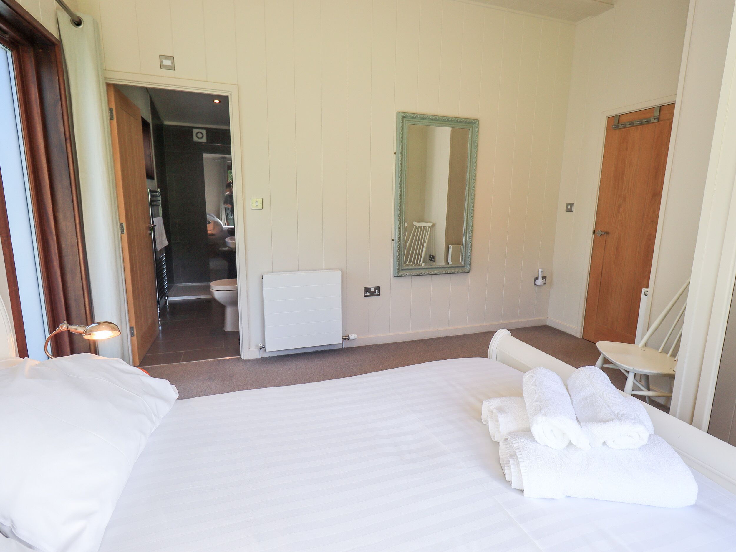 A hotel room with a large bed, a bathroom with a toilet and a mirror, and a chair.