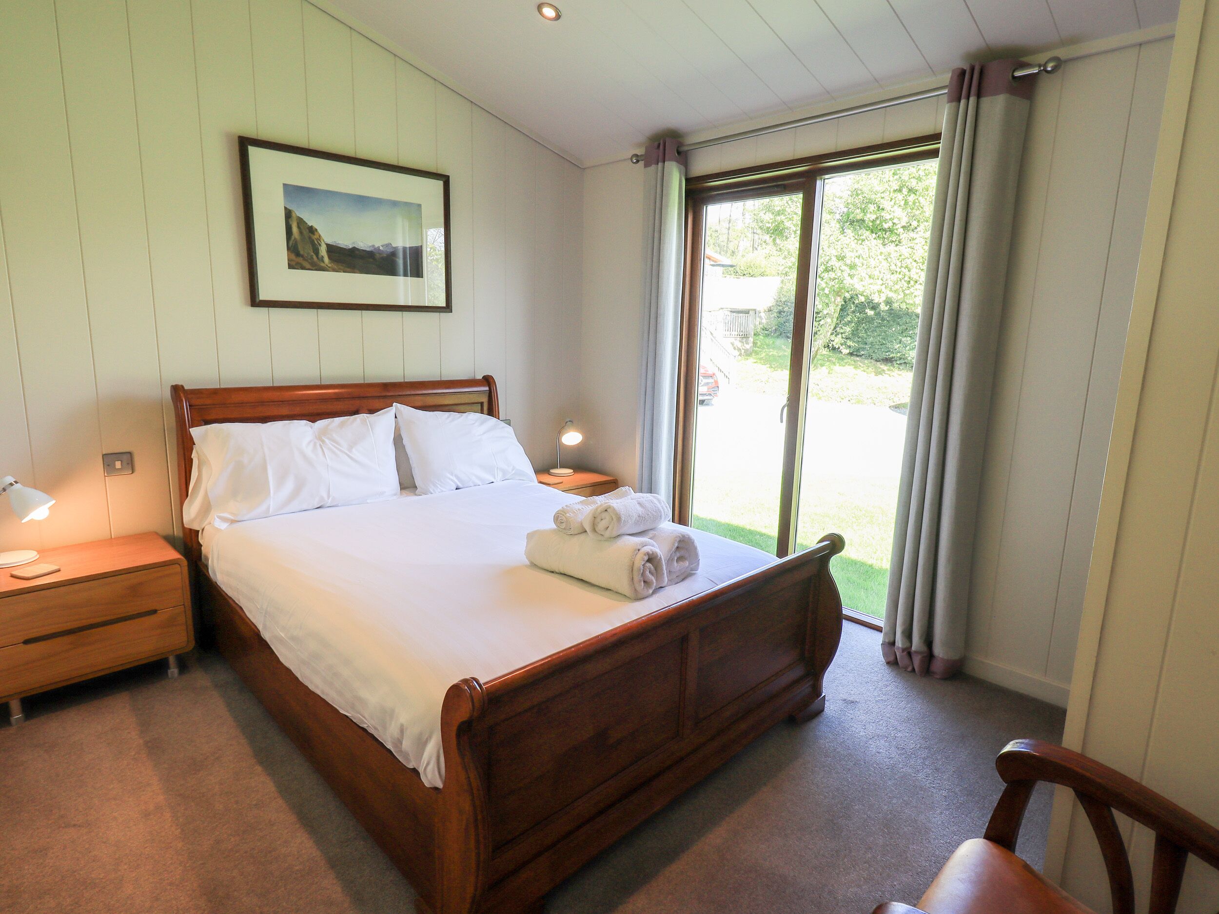 A neatly made bed with white linens, a wooden headboard, a bedside table with a lamp, and a framed picture on the wall.