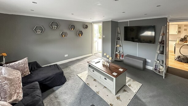 Una sala de estar moderna con un sofá gris, una mesa de centro blanca y un televisor de pantalla plana montado en la pared.
