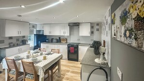 Una cocina moderna con armarios blancos, una mesa de comedor para cuatro personas y un horno empotrado.