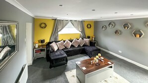 Una sala de estar moderna con un sofá negro, una mesa de centro de madera y un ventanal con cortinas.