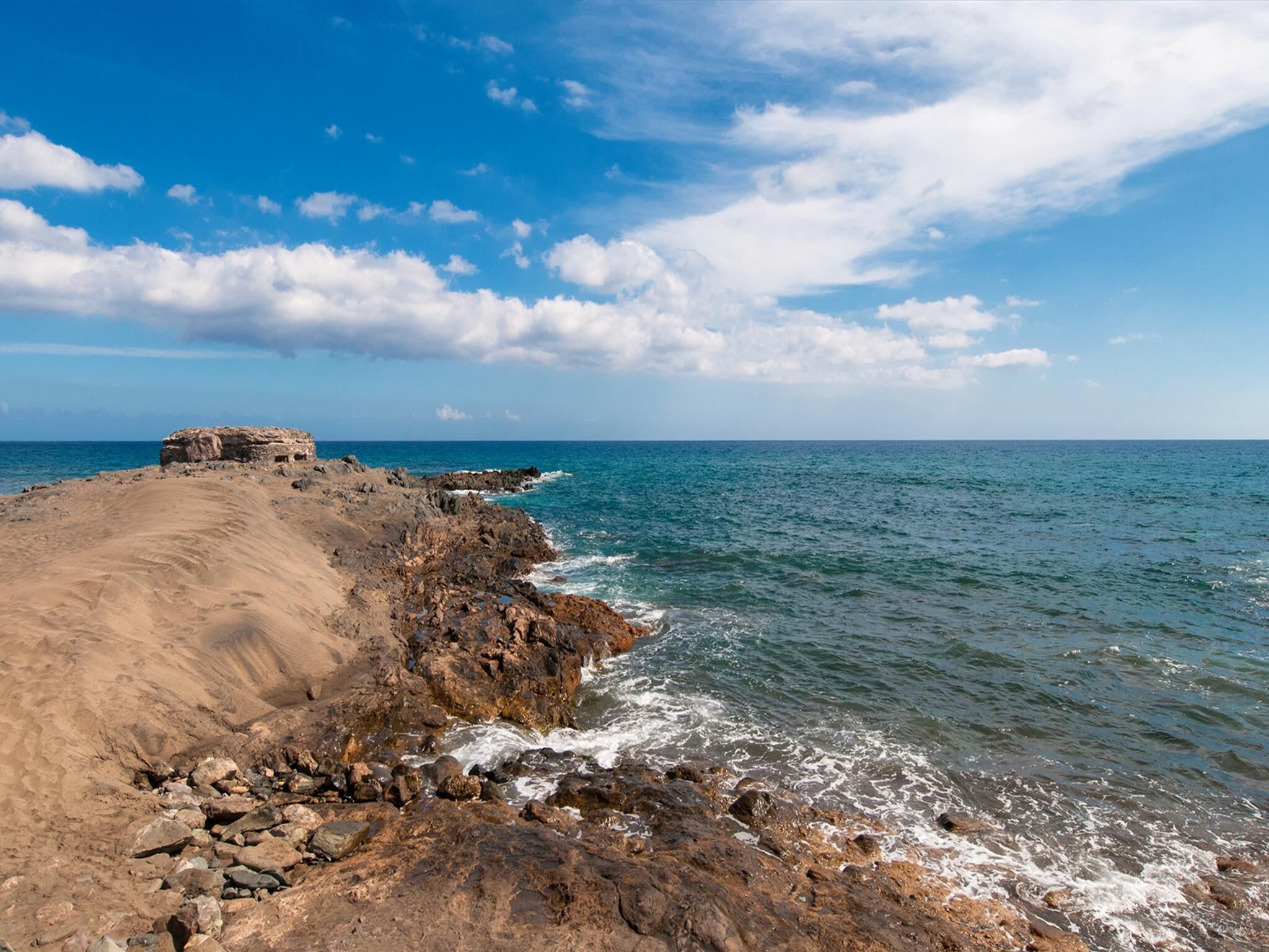 Un paisaje costero con costa rocosa, cielo despejado y mar tranquilo.