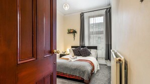 Una camera d'albergo con una porta in legno, un letto con copripiumino a quadri grigio e rosso, un poggiatesta bianco e una finestra con tende grigie.