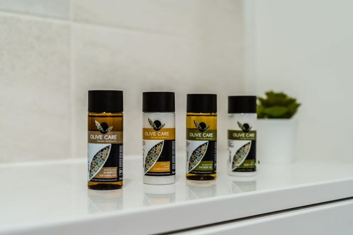 Four bottles of Olive Care hair care products on a white shelf.