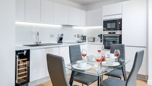 A modern kitchen with white cabinets, a built-in oven, and a dining area with a glass table and chairs. - Apollo Luxury - Netflix - Fast WIFI (West Midlands)