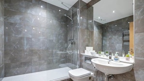 A modern bathroom with a glass-enclosed shower, a white bathtub, and a sink with toiletries. - Apollo Luxury - Netflix - Fast WIFI (West Midlands)